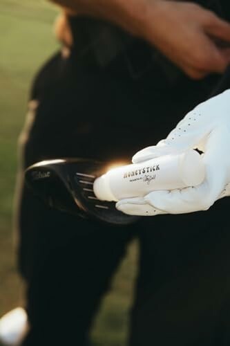 Person holding a golf club with a golf glove and a cylindrical object.