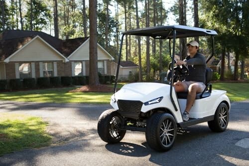 Person driving a white golf cart on a residential street.